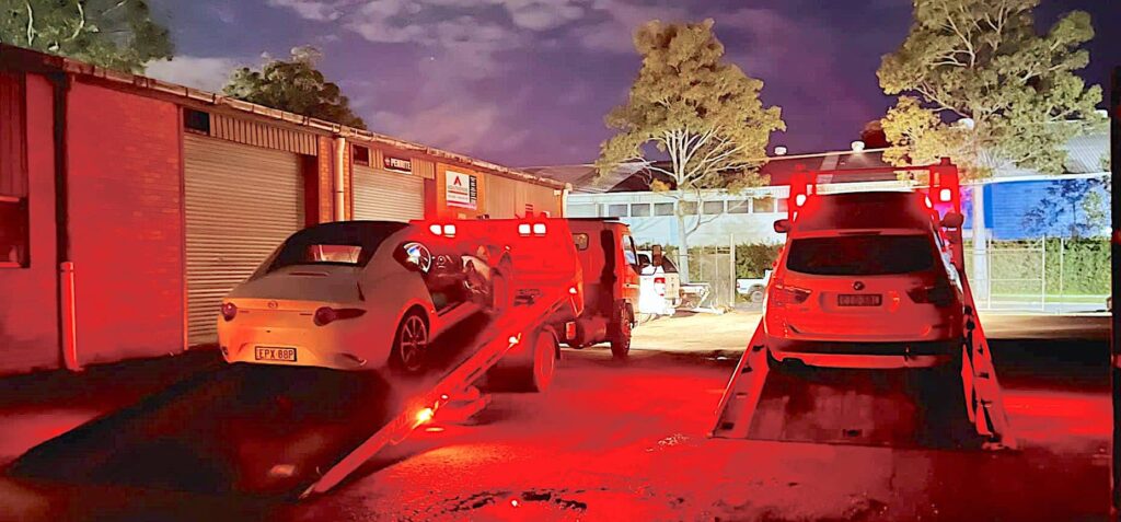 Two tilt tray towing truck picking up vehicles at night in Sydney.