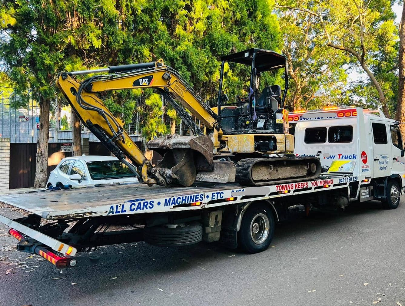 An excavator being towed by a tilt tray tow truck in Sydney.