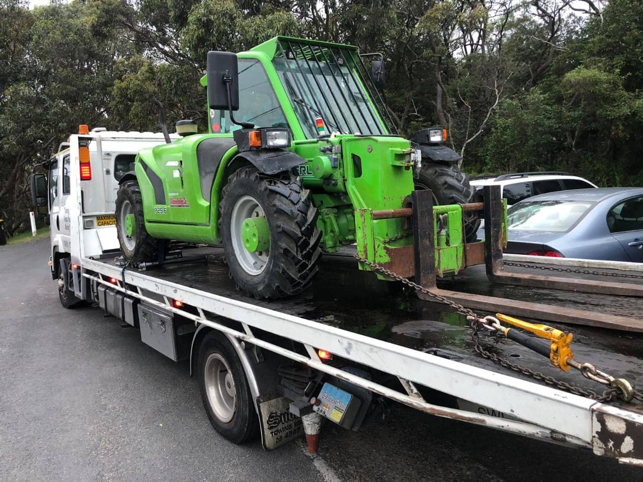 A telehandler fork lift being transported in Sydney by a tow truck.