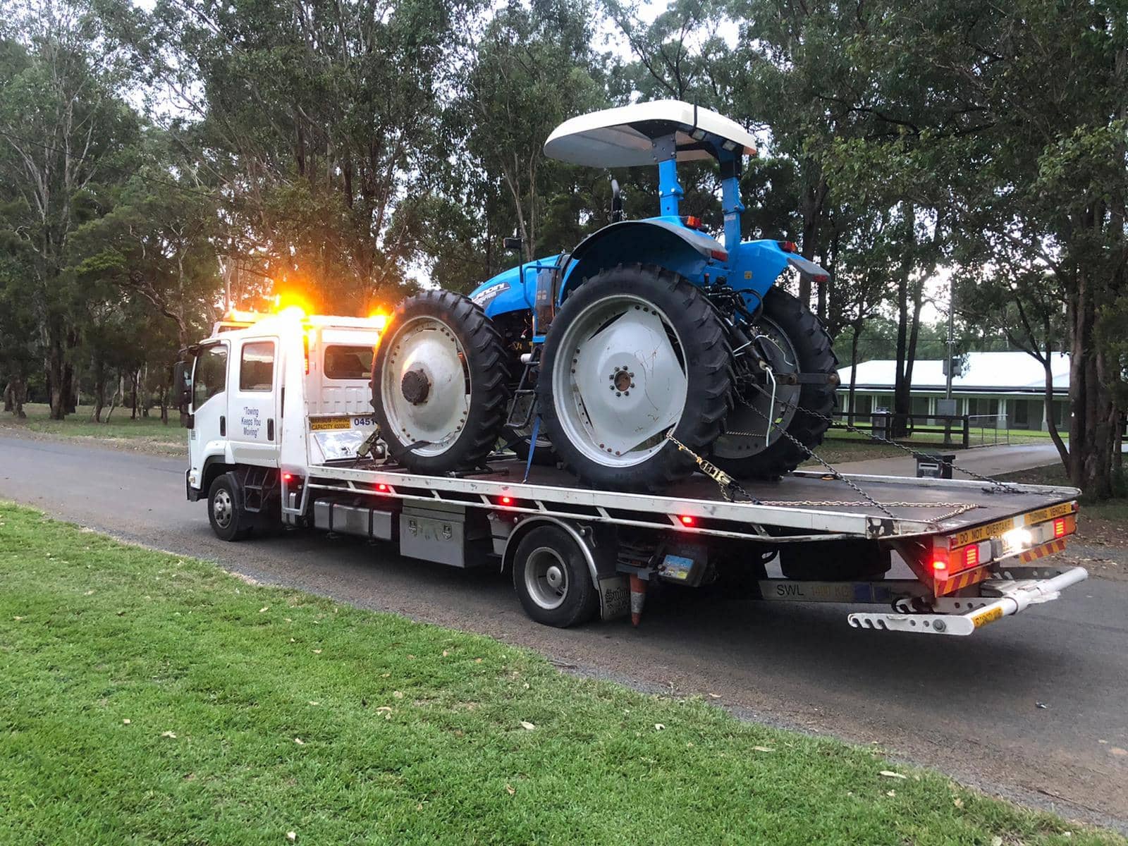 A large tractor on the back of a tilt tray tow truck.